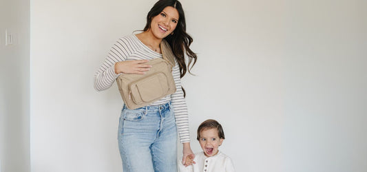 Mom wearing a beige Jetsetter Mini Diaper Bag crossbody while holding her toddler’s hand.
